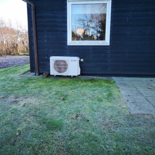 Udendørs varmepumpe ved sort træhus.