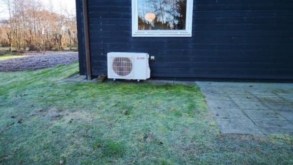 Udendørs varmepumpe ved sort træhus.